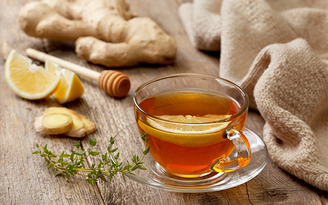 A cup of tea with lemon, a huge knob of ginger, honey, and herbs are pictured.