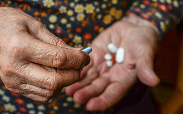 An elderly woman holds several pills in the palm of her hand.