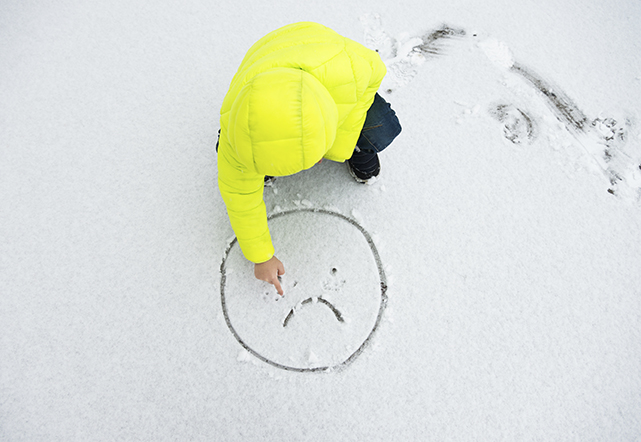 child drawing sad face in snow.