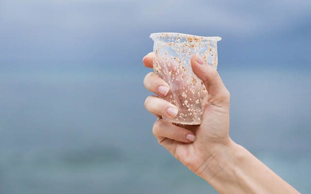 Hand holding plastic cup on beach