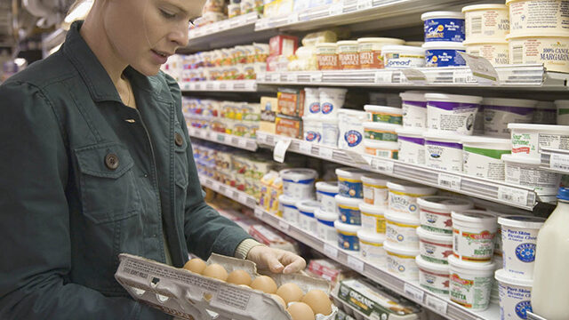 A woman looks at a carton of eggs in a grocery store.