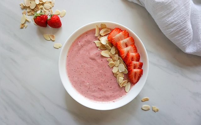 A strawberry-cheesecake smoothie bowl topped with sliced fresh strawberries and sliced almonds