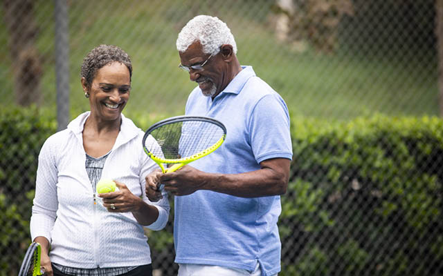An older African-American couple plays tennis.