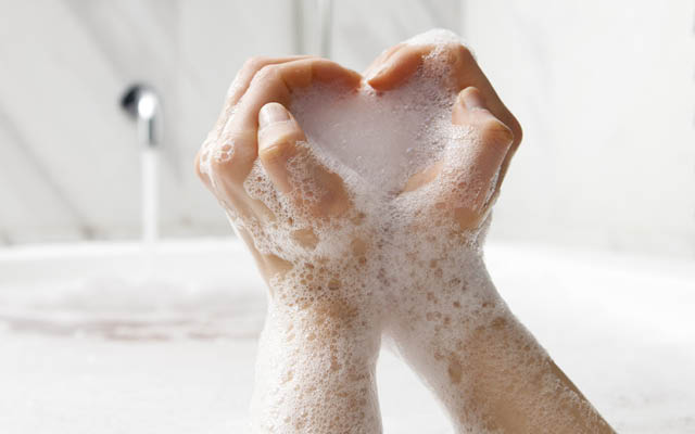 Soapy hands in a bath make a heart shape.