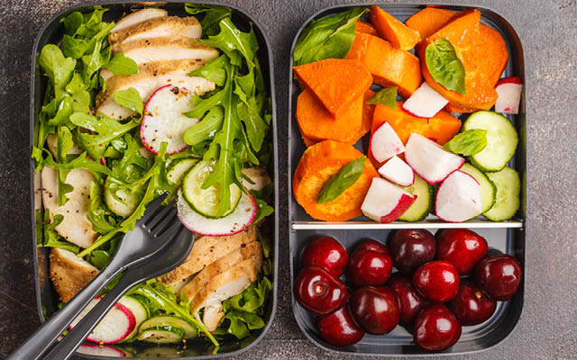 bento box filled with chicken, salad, and cherries.