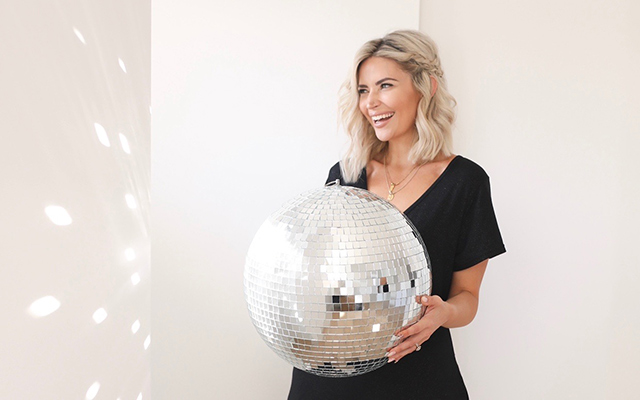 A woman holds a large disco ball.