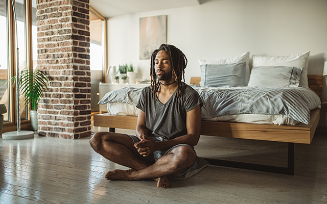 A Black man does yoga in his bedroom.