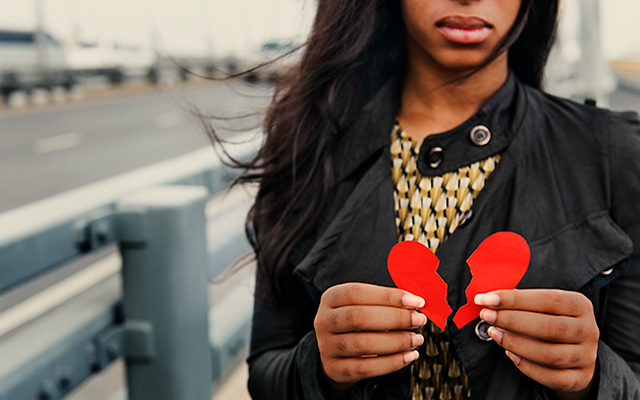 A Black woman holds a broken paper heart.