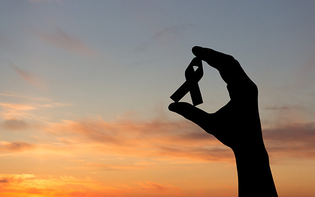 A hand in silhouette holds a cancer ribbon.