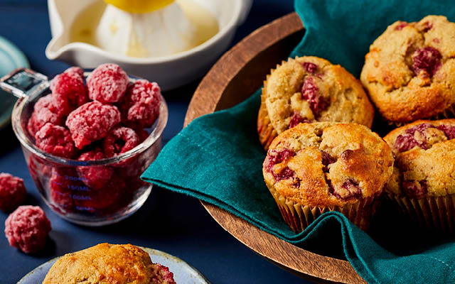 lemon raspberry muffins with a glass measuring cup filled with frosty raspberries