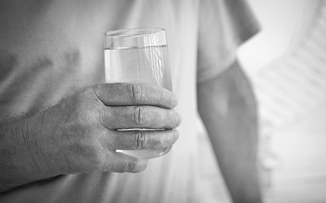 An elderly person holds a glass of water.