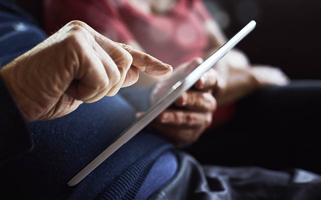 An elderly person looks at a digital tablet.