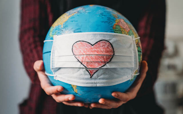 A person holds a globe that has a mask, with a drawing of a heart, on it.