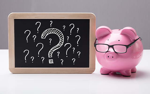 A piggy bank sits next to a small chalkboard filled with question marks.
