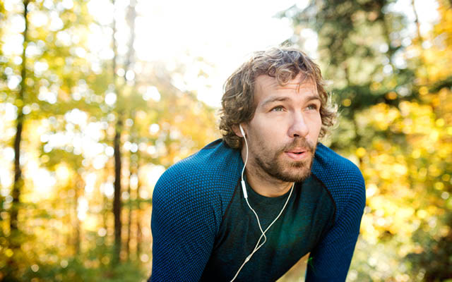 a man stops to exhale while running on a wooded trail