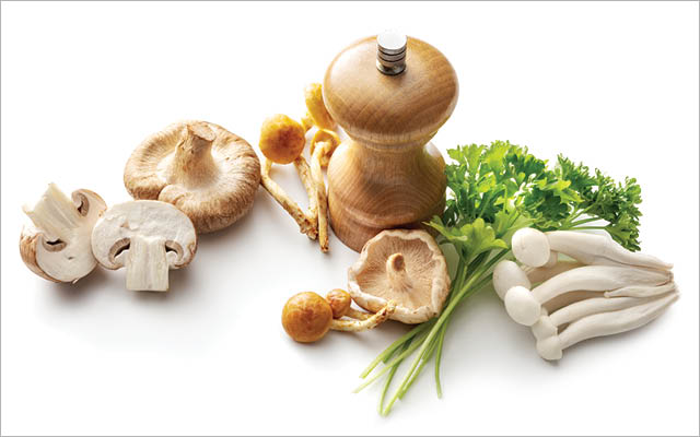 various mushrooms and sprigs of parsley placed around a wooden pepper grinder