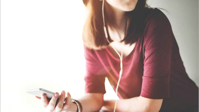 A woman listens to her phone via earbuds.