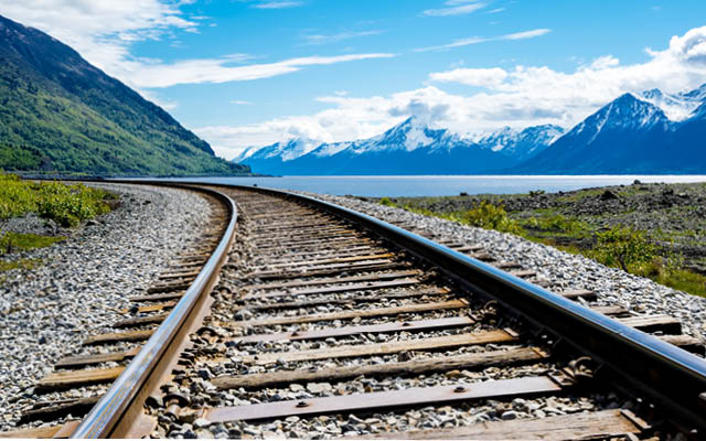 A photo of empty railroad tracks on a sunny day with mountains in the distance