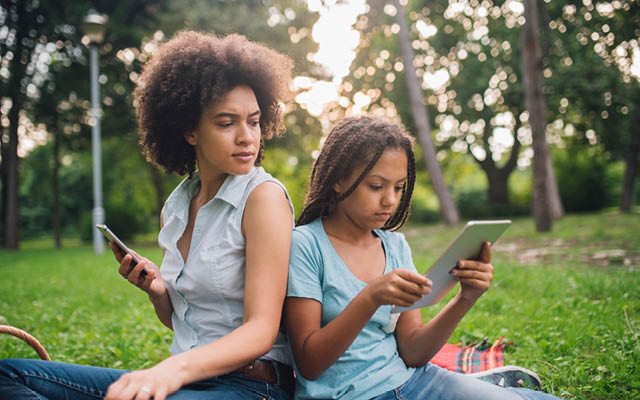 A mother and daughter are both on devices.