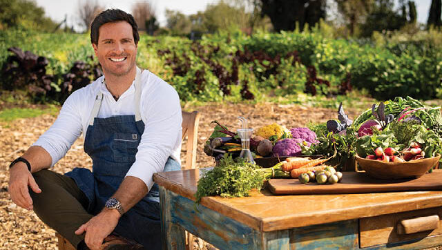 Chef Seamus Mullen smiles next to a table of veggies.