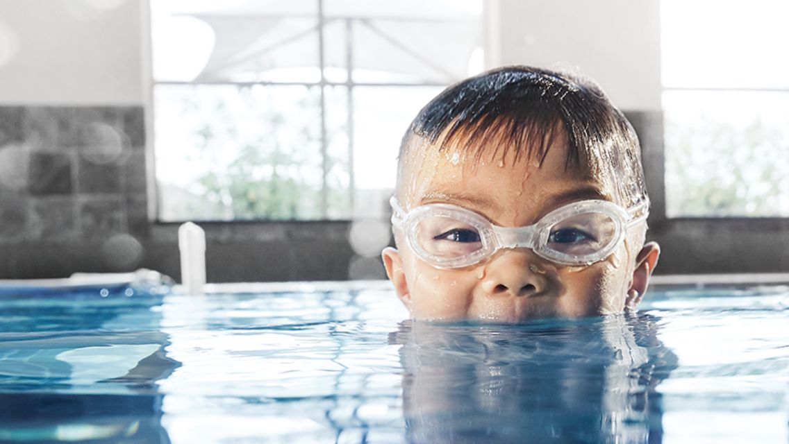 young boy with goggles peaking out of water