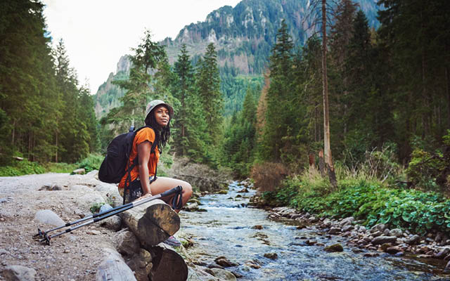 Person sitting by river with trekking poles