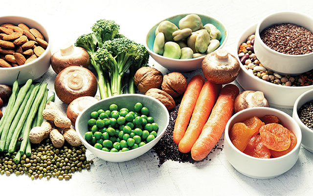 A variety of high-fiber foods, including peas, carrots, and broccoli, are pictured.