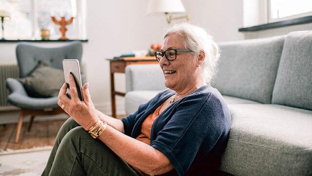 An older woman smiles as she looks at her cellphone.