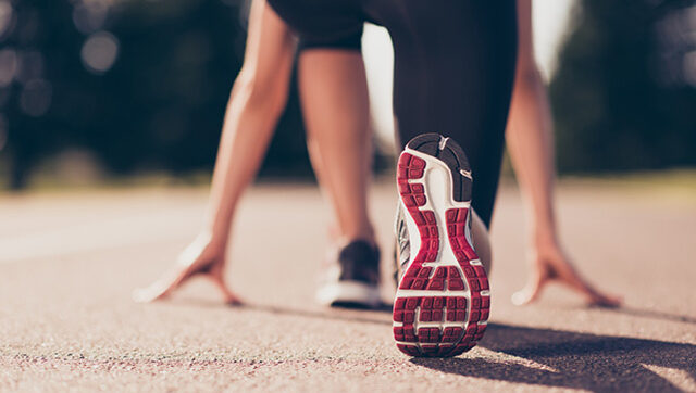 Close up cropped low angle photo of shoe of female athlete on the starting line of a stadium track, preparing for a run.