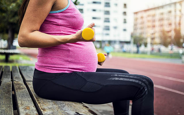 Pregnant woman sitting on bench lifting weights