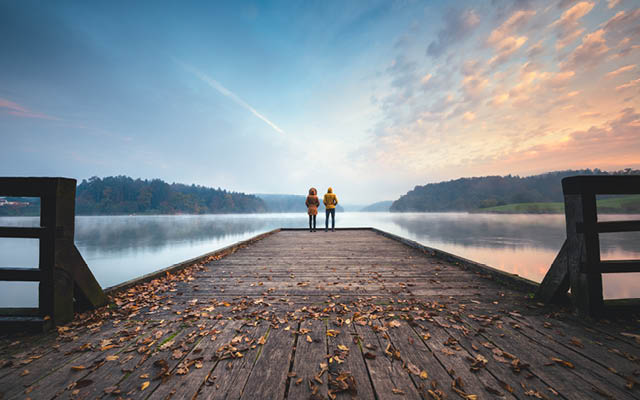 Two people at the end of a dock overlooking lake