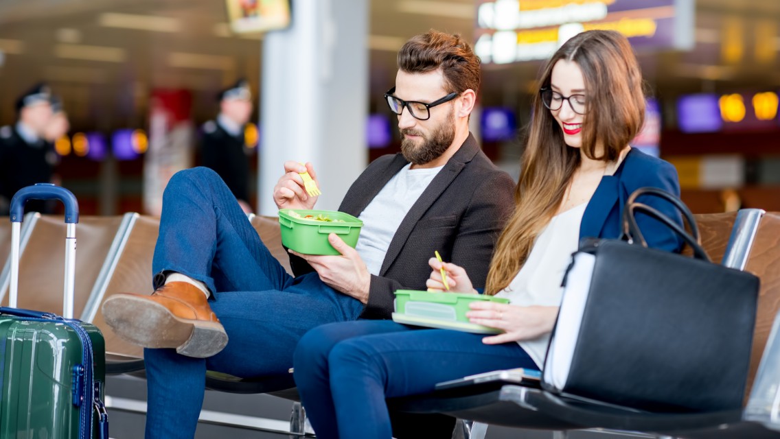 A man and a woman in an airport eating a meal.