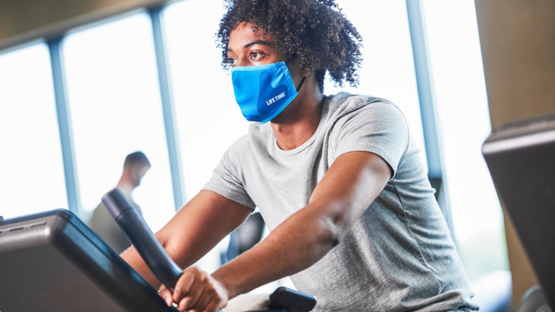 A person wearing a face mask on an exercise machine in a fitness club.
