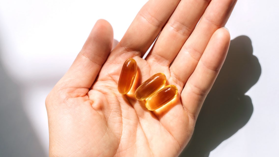 A person's hand holding three fish oil capsules.
