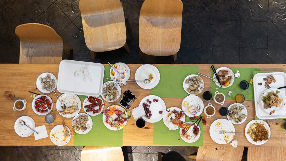 overhead view of a long kitchen table filled with plates of uneaten food with chairs pushed away