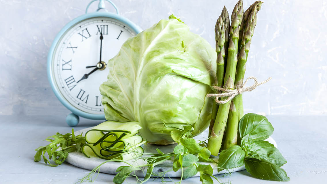 a clock sits behind an array of green veggies