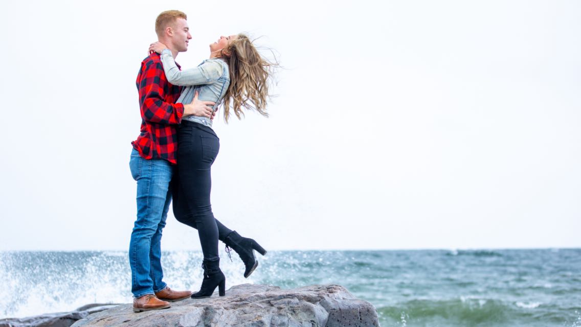 Michael and Marisa Pender embracing each other on a rock in front of a body of water.