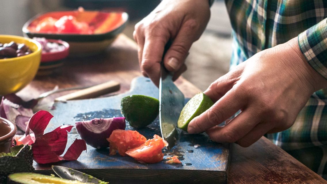 a close up of a man cutting a lime, onions and tomato
