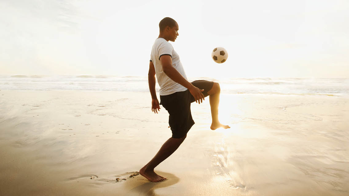 a man juggles a soccer ball on a beach
