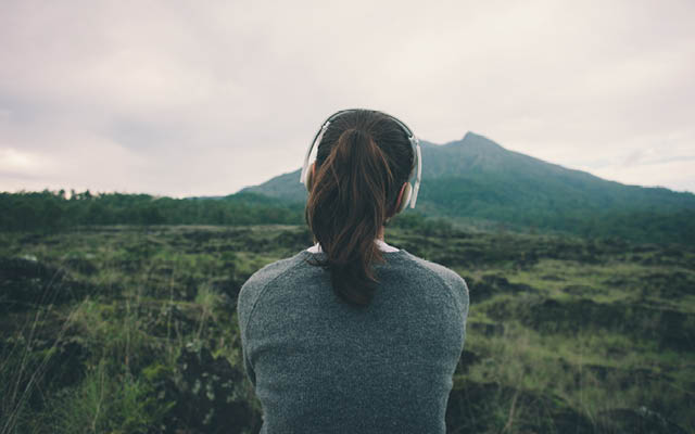 a woman wears headphones while looking at a mountain