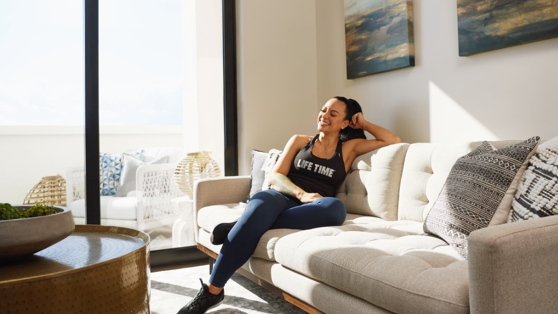 A woman smiling while sitting on the couch in a Life Time Living apartment.