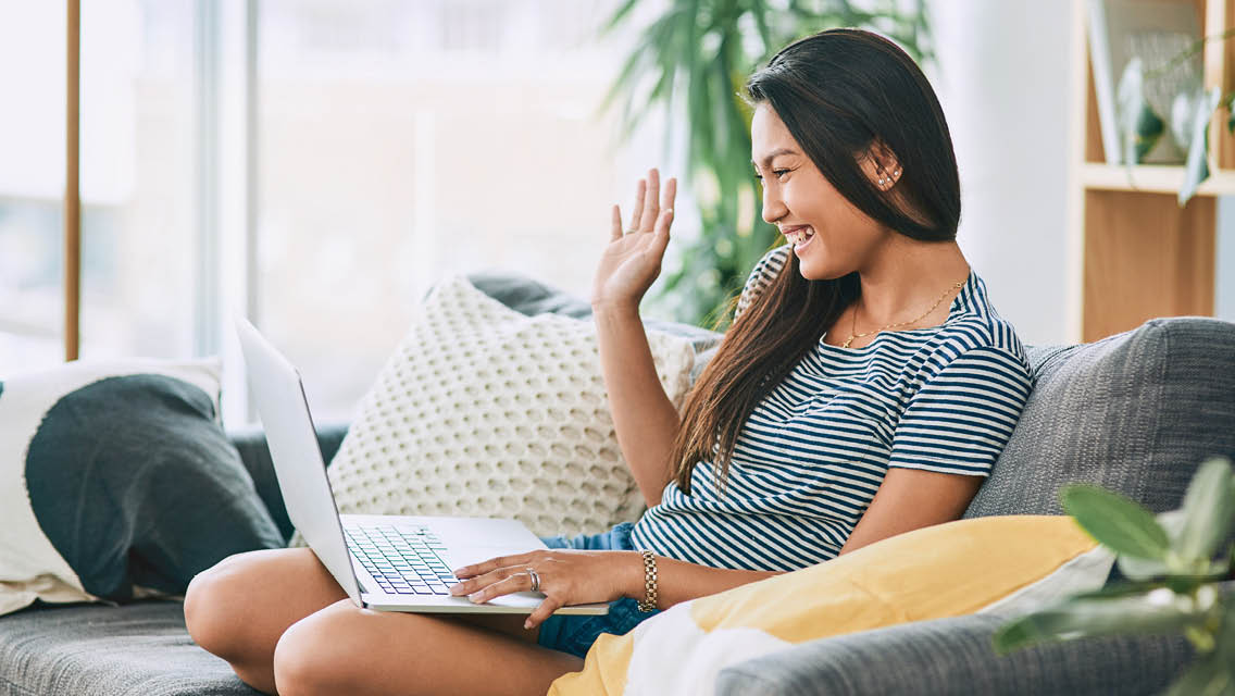 a woman smiles and waves to someone she's talking to via the computer