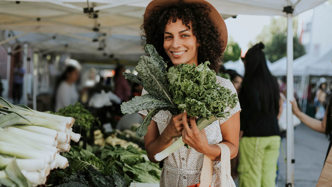 a woman holds a bunch of kale at a farmers market