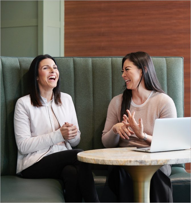 Two women laughing while working in a Life Time Work space.