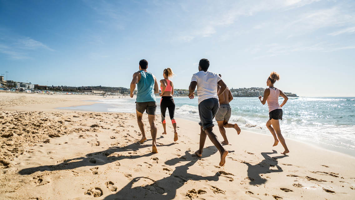 a group of people jogging barefoot on a beach