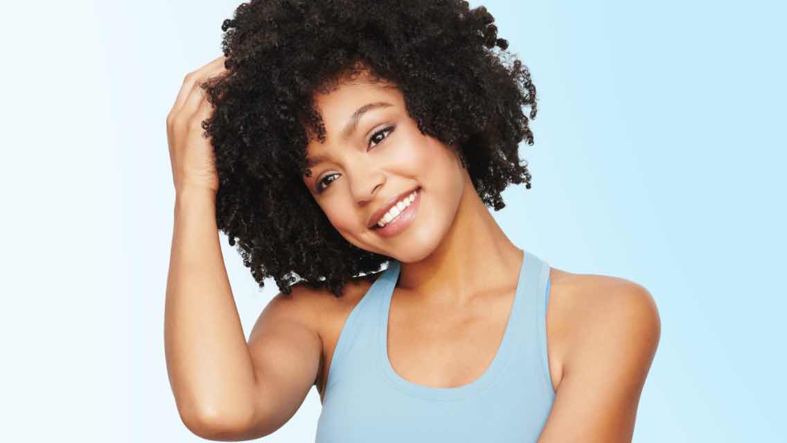 A woman smiling with voluminous, curly hair.