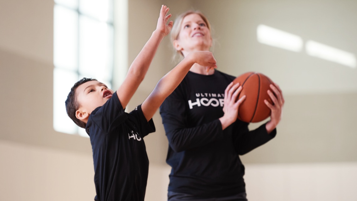 An adult woman and a young boy playing basketball together.