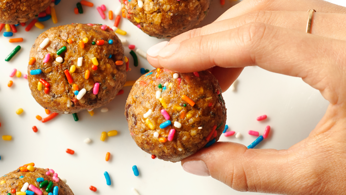 A person's hand holding up one of many Birthday Cake Protein Balls.