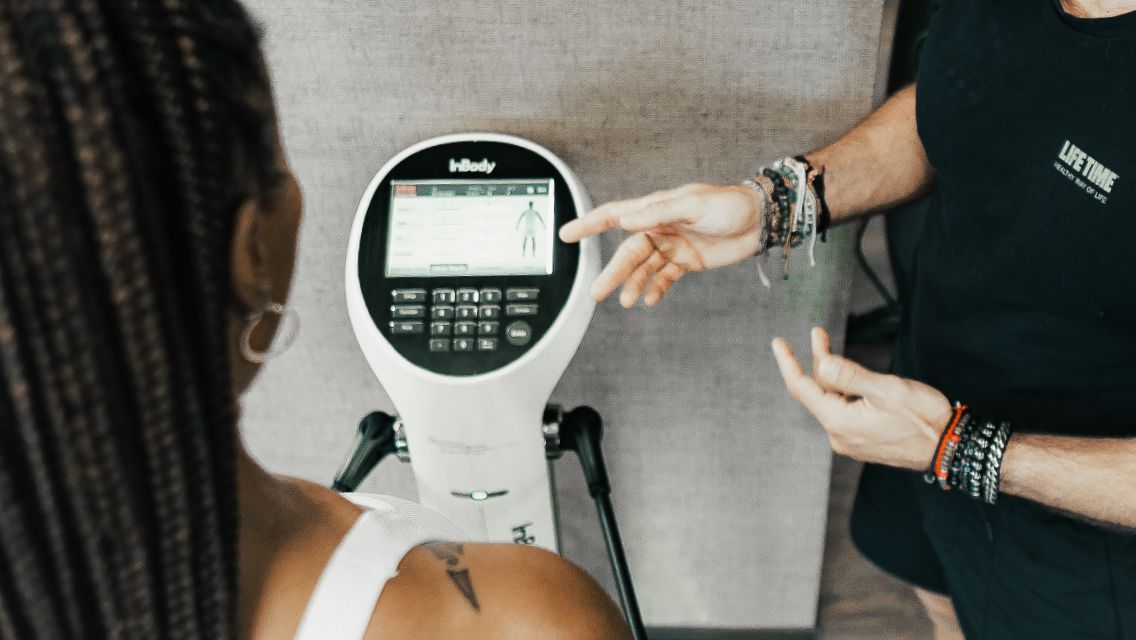 A trainer assisting a client with using the InBody scale at Life Time.