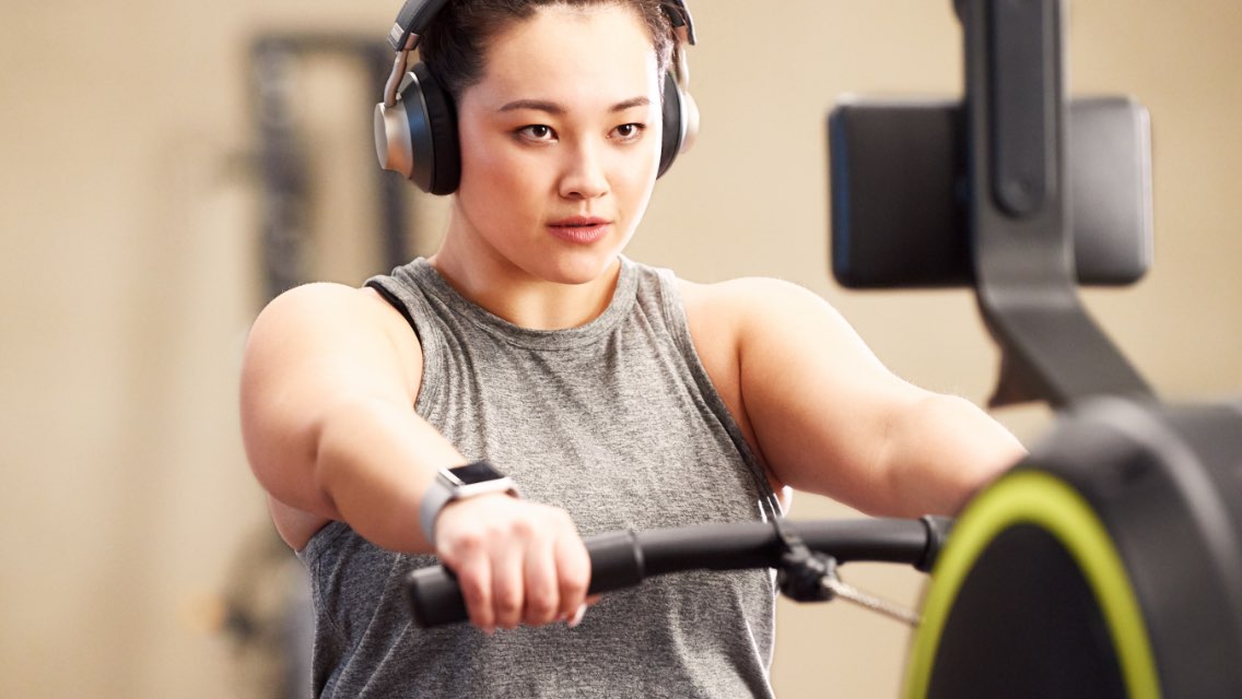 A woman with headphones on using a rower in a fitness facility.